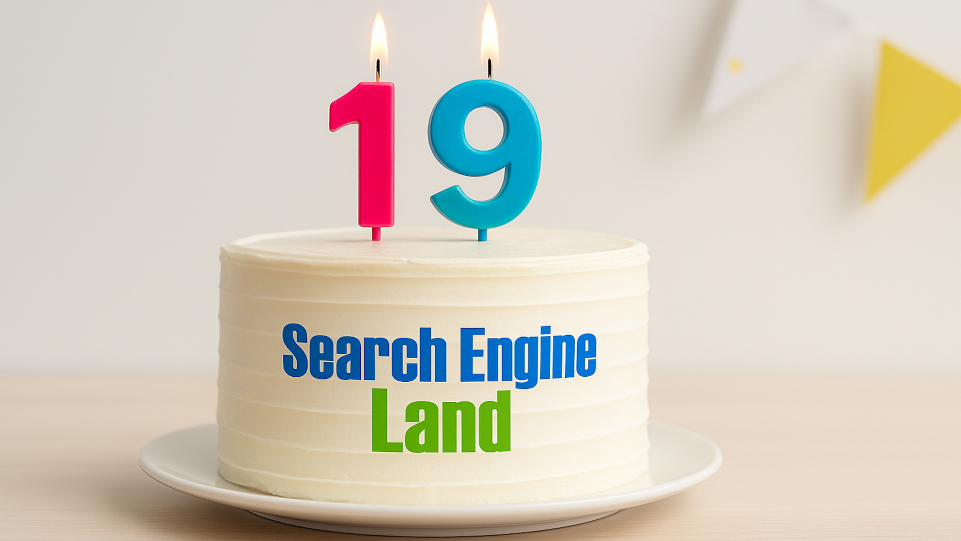 ```json
{
  "alt": "White frosted cake with 'Search Engine Land' text and lit number 19 candles on top.",
  "caption": "Celebrating 19 years! A beautifully frosted cake with lit candles marks a special anniversary for Search Engine Land.",
  "description": "A white frosted cake sits elegantly on a white plate, featuring the text 'Search Engine Land' in blue and green. Atop the cake are lit numerical candles forming the number 19, symbolizing an anniversary celebration. The background is softly blurred with a hint of festive bunting, adding a touch of celebration. Ideal for use in articles or blogs about anniversaries, celebrations, or Search Engine Land milestones."
}
```