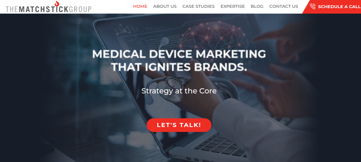 ```json
{
  "alt": "Medical device marketing advertisement with a laptop and network graphic overlay.",
  "caption": "Discover innovative medical device marketing strategies that ignite brands. Ready to elevate your brand? Let's talk!",
  "description": "This image features a marketing advertisement by The Matchstick Group, showcasing a focus on medical device marketing. A hand points towards a laptop screen with technological graphics, symbolizing strategy at the core of brand development. The call-to-action button 'Let's Talk!' invites engagement. Keywords: medical device marketing, brand strategy, innovation."
}
```