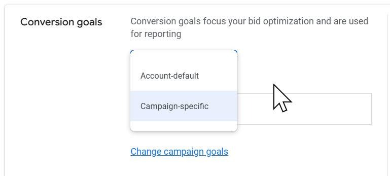 ```json
{
  "alt": "Dropdown menu for selecting conversion goals in a digital marketing interface.",
  "caption": "Choose between account-default or campaign-specific conversion goals to optimize your digital marketing strategy.",
  "description": "This image shows a dropdown menu interface in a digital marketing platform where users can select conversion goals, either 'Account-default' or 'Campaign-specific'. A cursor is pointing at 'Campaign-specific'. This selection affects bid optimization and reporting strategies. Keywords: conversion goals, bid optimization, digital marketing, dropdown menu, campaign management."
}
```